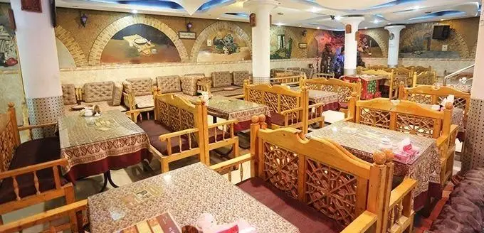 فضای داخلی رستوران و سفره خانه مجنون با دکوراسیون سنتی و اصیل، میز و صندلی‌های چوبی منبت‌کاری شده و تخت‌های راحت برای مهمانان.