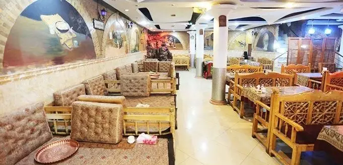 تصویر فضای داخلی رستوران و سفره خانه سنتی مجنون با مبلمان چوبی، نقاشی‌های دیواری و نورپردازی گرم، مکانی دنج برای لذت بردن از غذاهای اصیل ایرانی.