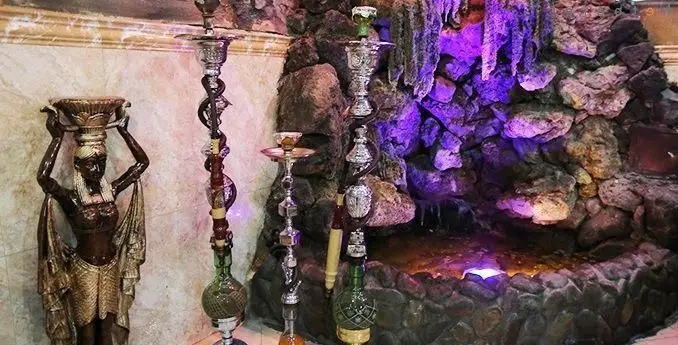 فضای داخلی رستوران و سفره خانه مجنون با دکوراسیون سنتی، مجسمه مصری، قلیان‌های زیبا و آبنمای صخره‌ای با نورپردازی بنفش.