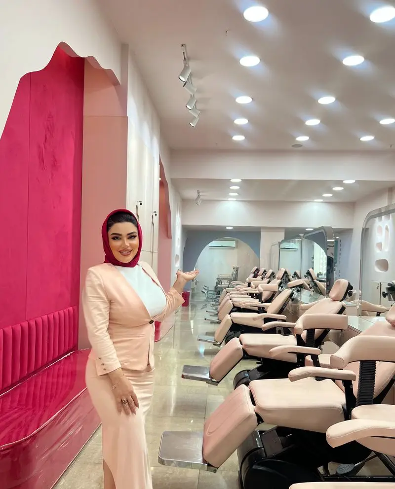 پرسنل سالن زیبایی با کت و دامن صورتی و شال قرمز در کنار صندلیهای مخصوص آرایش و اصلاح در سالن آرایشی مدرن و مجهز