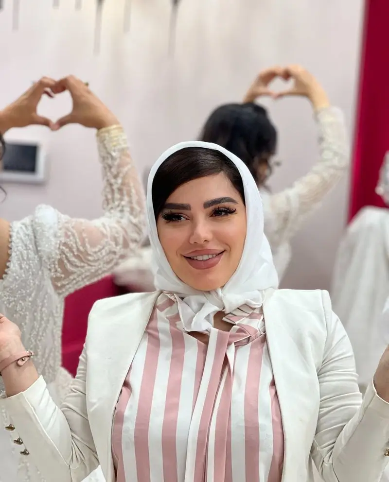 نمونه میکاپ و آرایش صورت زن جوان با شال سفید و کت مجلسی شیک در سالن زیبایی تخصصی عروس با بک گراند ژستهای قلب با دست