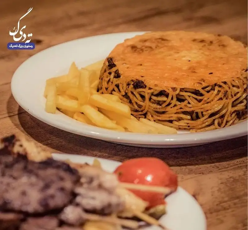 ماکارونی ته دیگ خوشمزه رستوران ته دیگ، با رویه طلایی و سیب زمینی سرخ کرده. در پس زمینه کباب های ایرانی نیز دیده می شود.