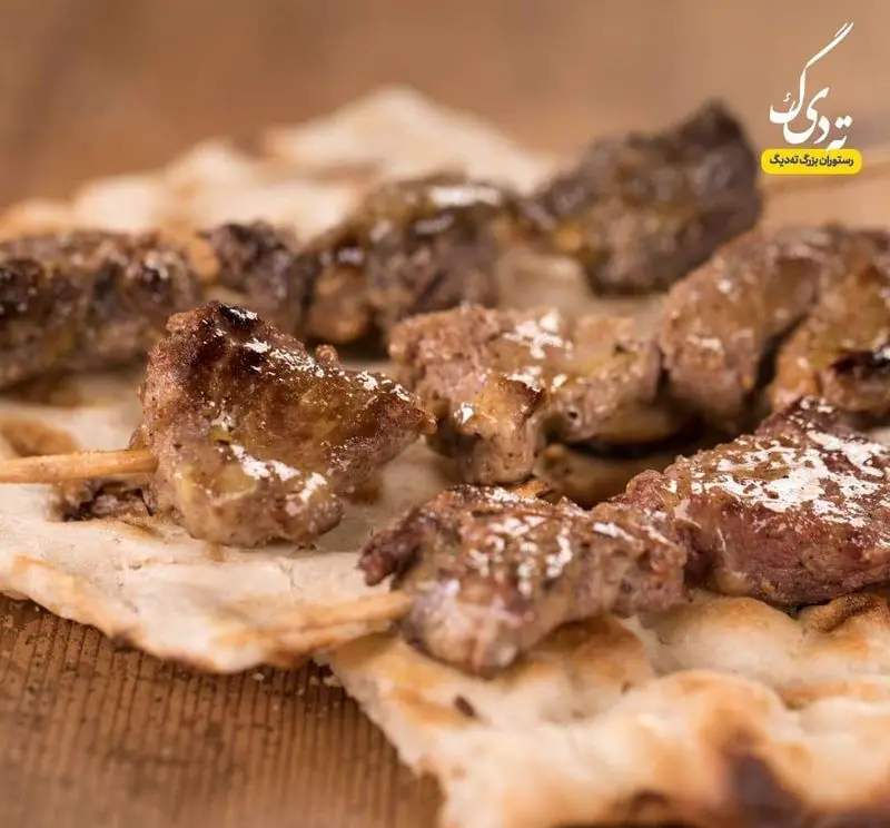 سیخ‌های کباب لذیذ جگر یا گوشت تازه، گریل شده و با سماق روی نان سنگک داغ، آماده در رستوران بزرگ ته دیگ. طعمی اصیل و فراموش‌نشدنی.
