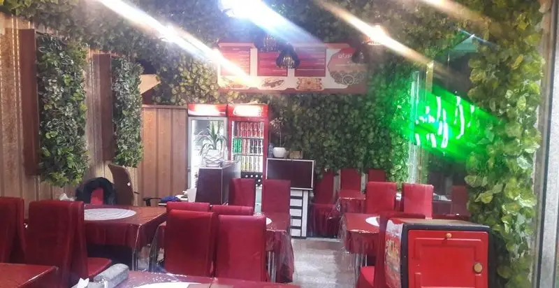 تصویری از فضای داخلی رستوران ته دیگ، دکوراسیونی دلنشین با برگ‌های سبز، میز و صندلی‌های قرمز، آماده پذیرایی از میهمانان.
