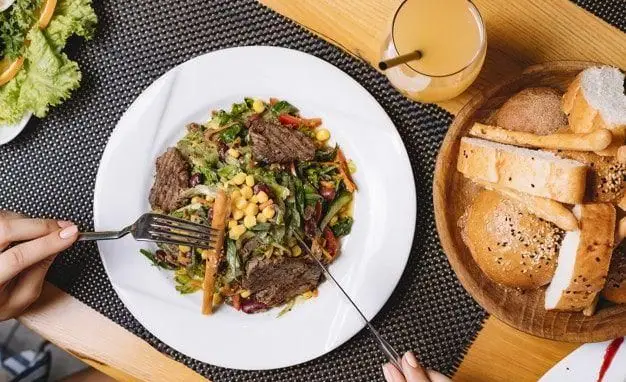 تجربه غذایی لذیذ از به پخت: سالاد استیک، ذرت و سبزیجات تازه، همراه با نان و آبمیوه، انتخابی عالی از تهیه غذا و فست فود.