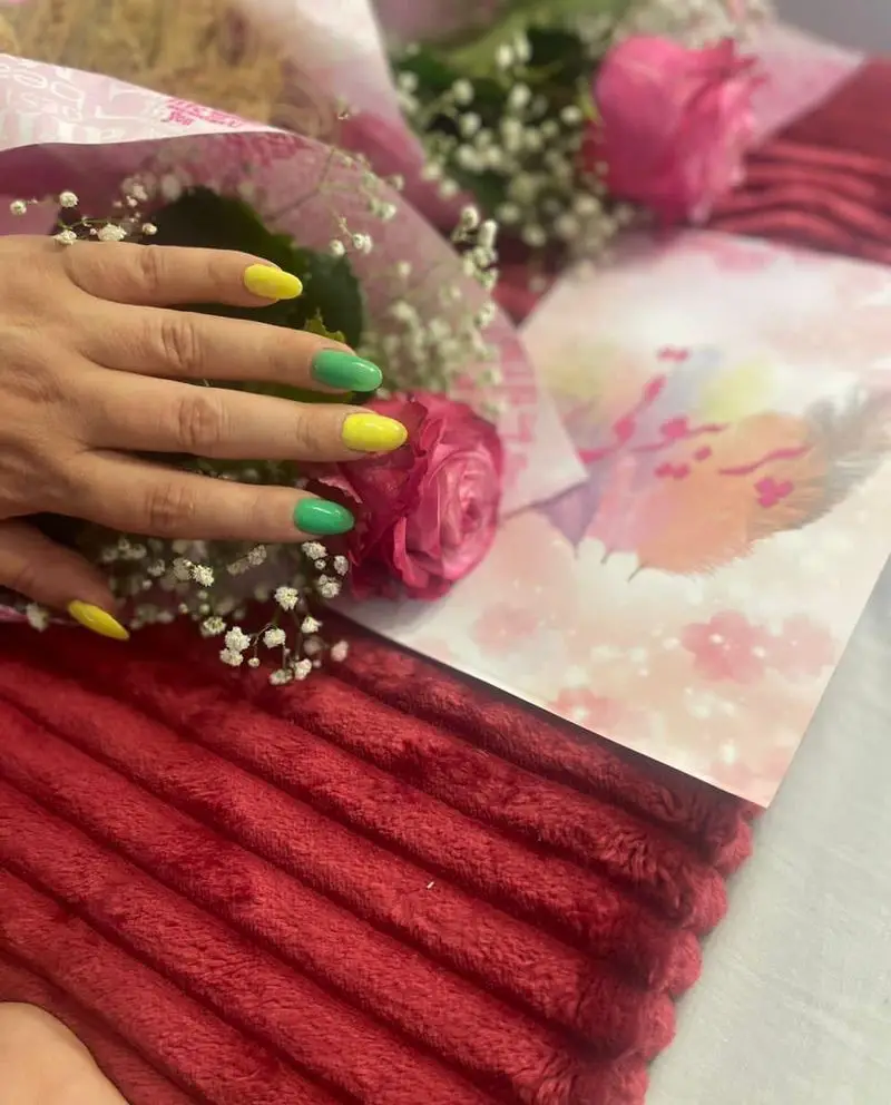 کاشت و طراحی ناخن با لاکهای زرد و سبز در سالن زیبایی پر بیوتی در کنار دسته گل رز صورتی زیبا روی پتوی قرمز رنگ