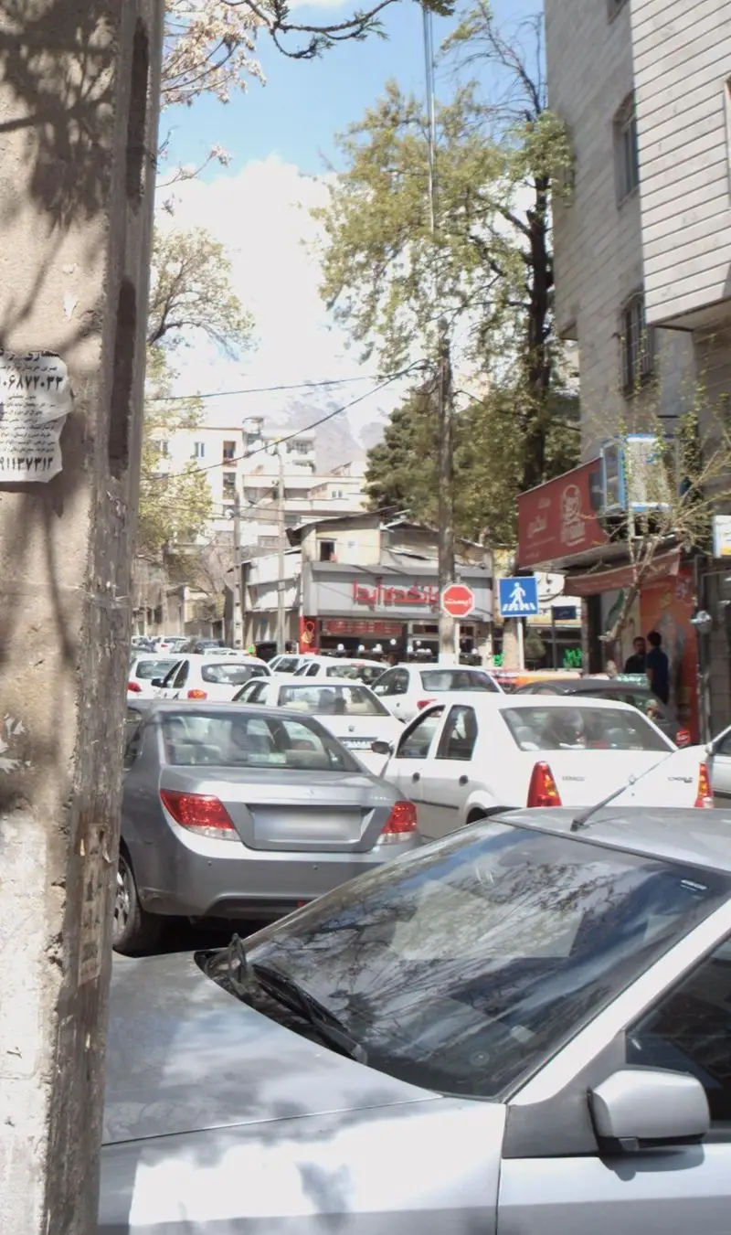 نمایی از خیابان شلوغ و پرترافیک که در آن بریانکده آیدا با تابلوی قرمز خودنمایی می‌کند. ماشین‌ها و ساختمان‌های شهری در کنار کوه‌های برفی.