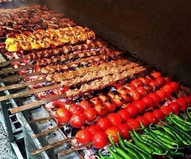 انواع کباب ایرانی (جوجه، کوبیده، گوشت) با گوجه و فلفل سبز تازه در حال پخت روی آتش، تجربه غذای اصیل در رستوران زیتون سبز.