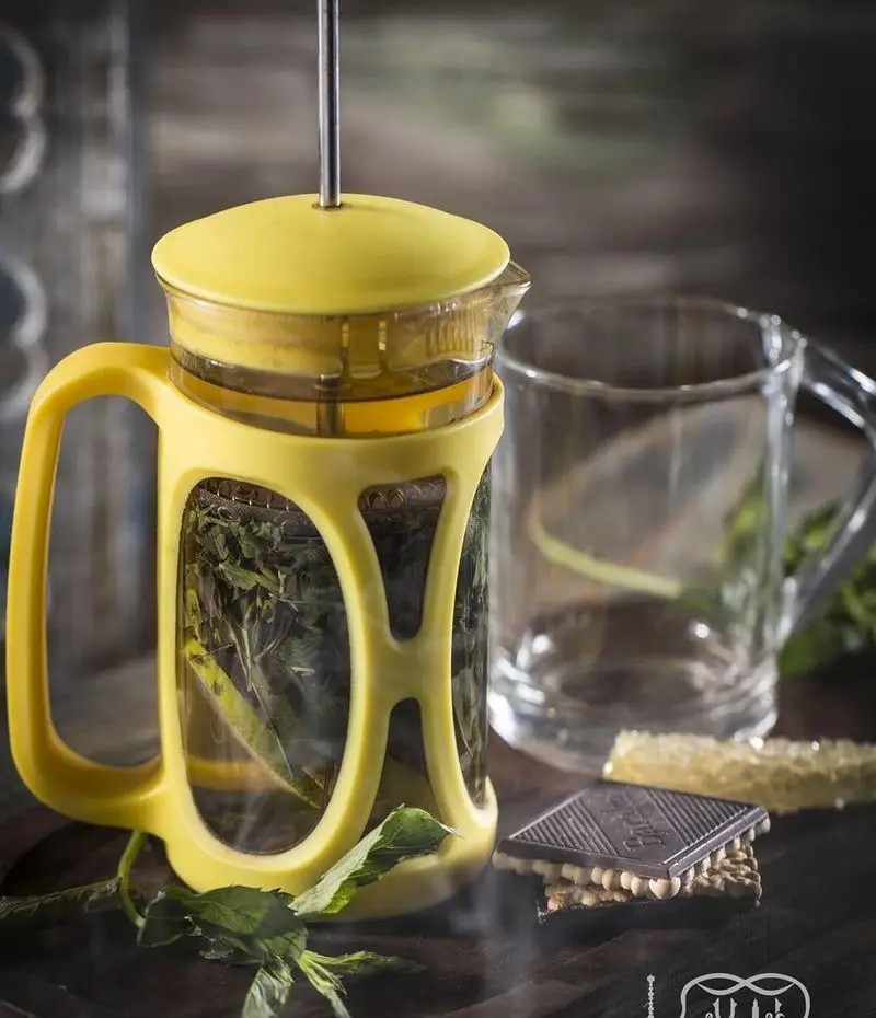 صحنه‌ای دلنشین از دمنوش نعناع در فرنچ پرس زرد، آماده سرو در کافه عربی کازابلانکا به همراه شکلات و عسل.