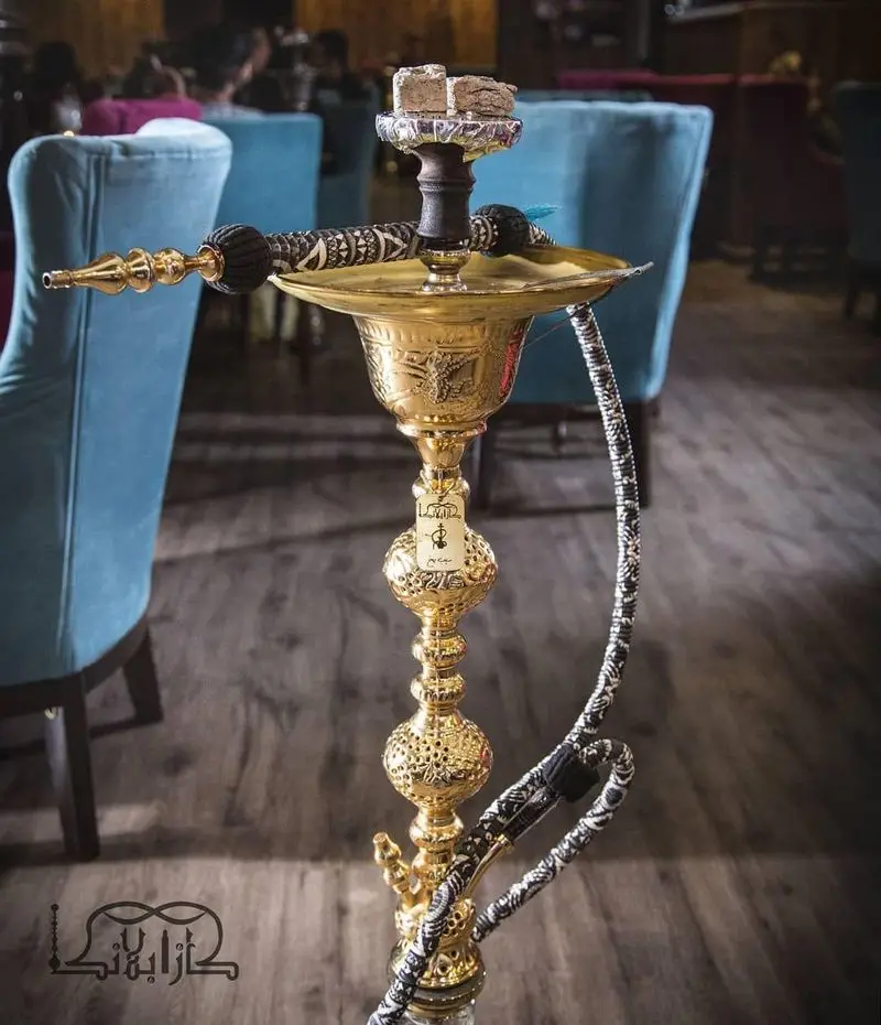 قلیان طلایی و مجلل کافه عربی کازابلانکا، با زغال‌های برافروخته، آماده برای تجربه‌ای لوکس و سنتی در فضای شیک ما.