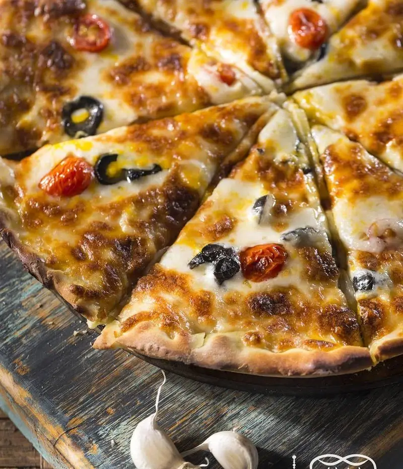 تصویری از پیتزای داغ و تازه با پنیر ذوب شده، گوجه گیلاسی و زیتون سیاه، آماده سرو در کافه عربی کازابلانکا. تجربه طعم بی‌نظیر.