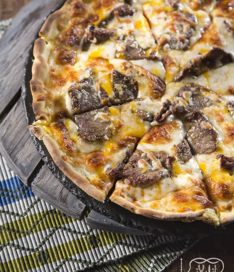 پیتزا گوشت و پنیر طلایی و خوشمزه کافه عربی کازابلانکا، آماده سرو روی میز چوبی، تجربه‌ای بی‌نظیر از طعم اصیل.