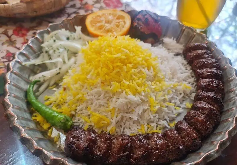 کباب کوبیده اصیل و برنج زعفرانی خوش‌عطر، همراه با فلفل سبز و مخلفات تازه در بشقاب سنتی از رستوران مرشد نیاوران.