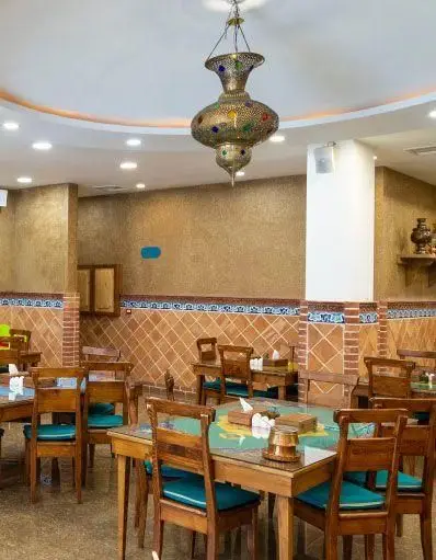 فضای داخلی گرم و دلنشین رستوران مرشد نیاوران با چیدمان سنتی، لوستر ایرانی چشمگیر، میزهای چوبی و کاشی‌کاری‌های اصیل برای تجربه‌ای خاص.