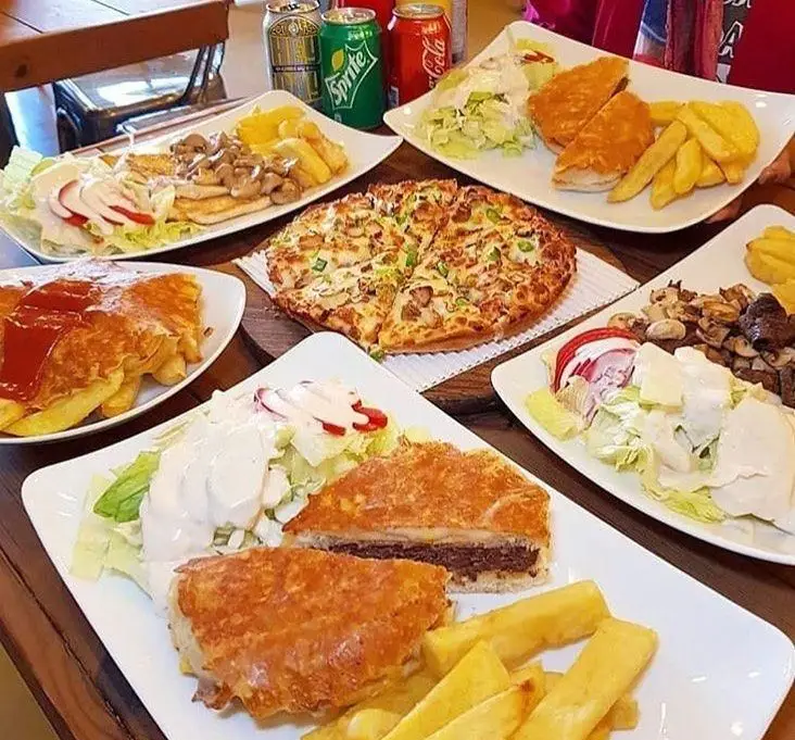 میز متنوع فست فود ترنج شعبه ۳ با پیتزا، شنیسل، سیب زمینی سرخ کرده، سالادهای تازه و ساندویچ‌های خاص با نوشیدنی.
