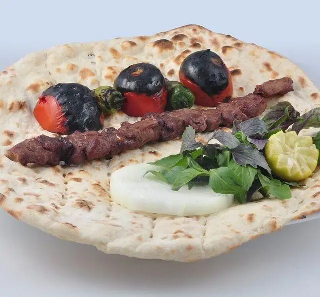 تصویر کباب کوبیده مخصوص کباب سرای برگ سبز با نان داغ، گوجه و فلفل کبابی، پیاز، ریحان تازه و برش لیمو. غذای اصیل ایرانی.