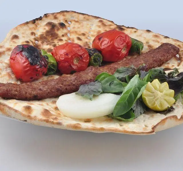 کباب کوبیده مخصوص کباب سرای برگ سبز روی نان، همراه با گوجه و فلفل کبابی، سبزی خوردن تازه، پیاز و لیمو. غذای اصیل ایرانی.