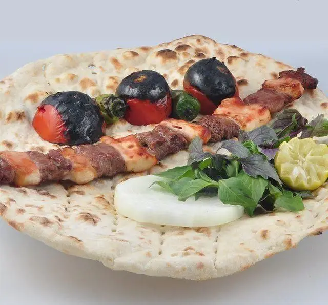 کباب مخلوط لذیذ برگ سبز شامل گوشت و گوجه کبابی روی نان داغ، همراه سبزی تازه و پیاز. تجربه غذای سنتی ایرانی.