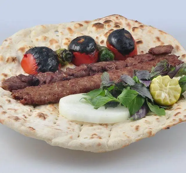 کباب کوبیده مخصوص کباب سرای برگ سبز با نان تازه و داغ، گوجه و فلفل کبابی آبدار، به همراه ریحان و پیاز و لیمو ترش برای یک تجربه غذایی بی‌نظیر.