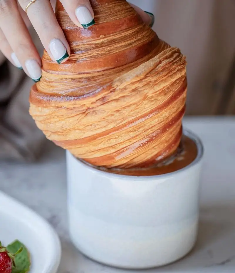 کروسان طلایی و ترد در حال غوطه ور شدن در قهوه یا لاته، تجربه‌ای شیرین در کافه رستوران رنسانس برای صبحانه.