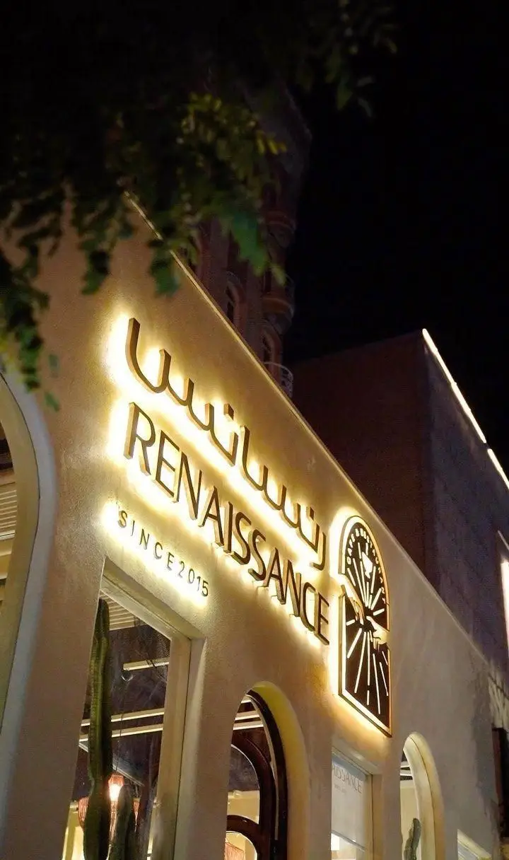 نمای شب کافه رستوران رنسانس با تابلوهای درخشان و لوگوی ساعت، طراحی شیک و نورپردازی جذاب. تاسیس 2015.