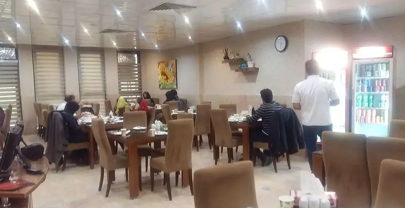 تصویری از داخل رستوران ایرانی اصل جوان، با محیطی دلنشین و میز و صندلی‌های مدرن، مشتریان در حال لذت بردن از غذای اصیل ایرانی.