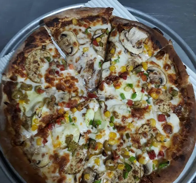 پیتزا سبزیجات خوشمزه و رنگارنگ از پیتزا و کباب ترکی علی بابا با قارچ، ذرت، فلفل و زیتون، آماده سرو روی سینی.