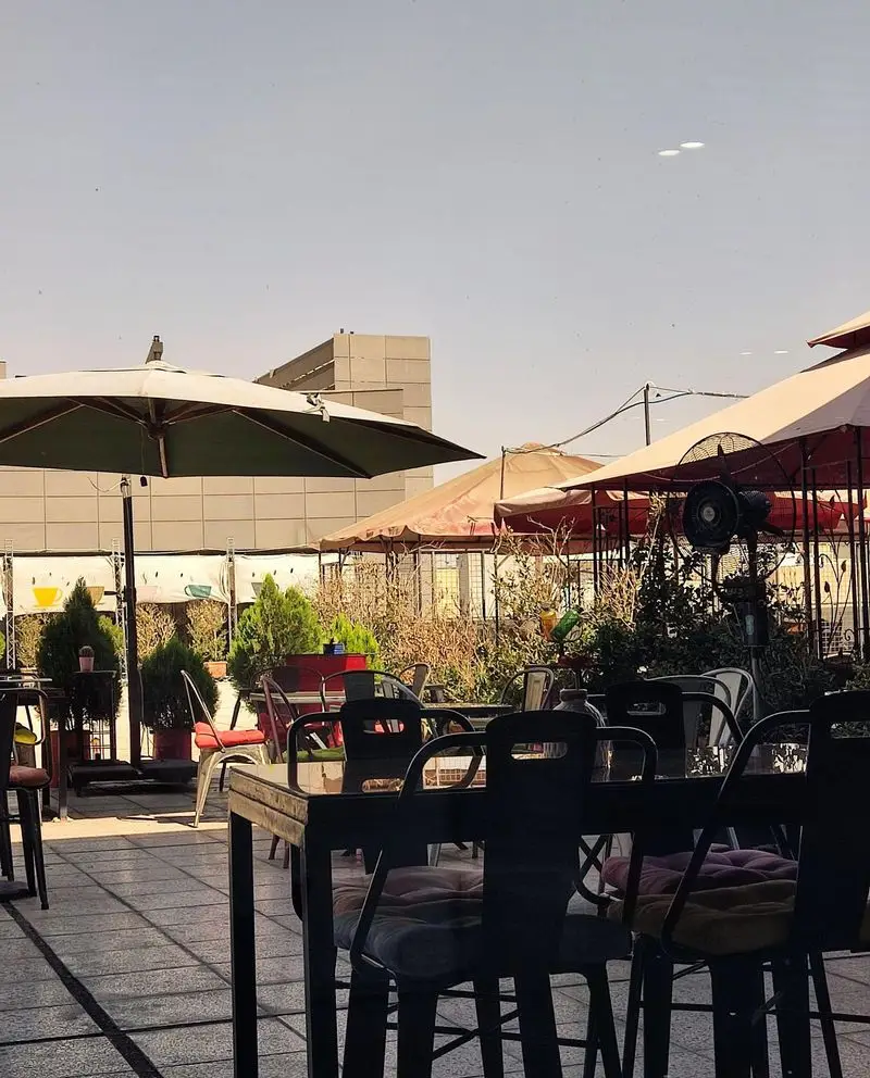 کافه رستوران نسکو: نمای جذاب از فضای باز و محیط دلنشین با میز و صندلی‌های شیک، چترهای آفتابگیر و گیاهان سرسبز، مناسب دورهمی‌های دوستانه.