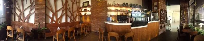 تصویری پانوراما از فضای دنج کافه رستوران نسکو با دکوراسیون چوبی، دیوار آجری، میز و صندلی‌های راحت و بار مجهز قهوه و نوشیدنی