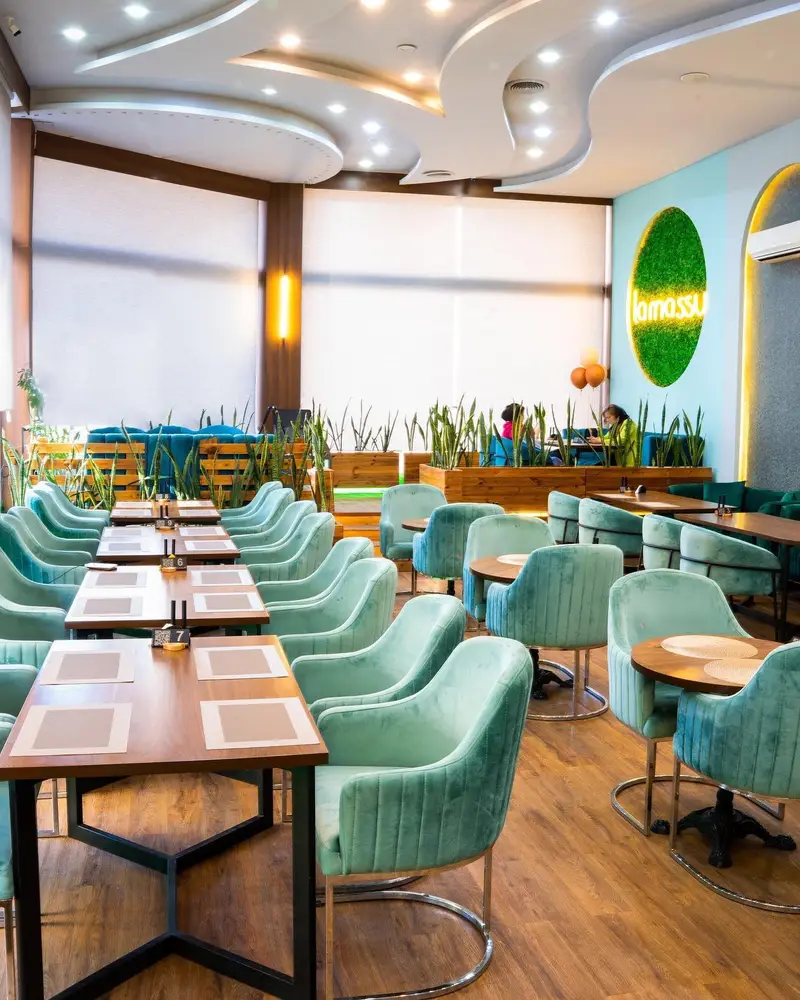 تصویری از فضای داخلی شیک و مدرن کافه رستوران لاماسو با صندلی‌های مخملی سبزآبی، میزهای چوبی و سقف منحصر به فرد.