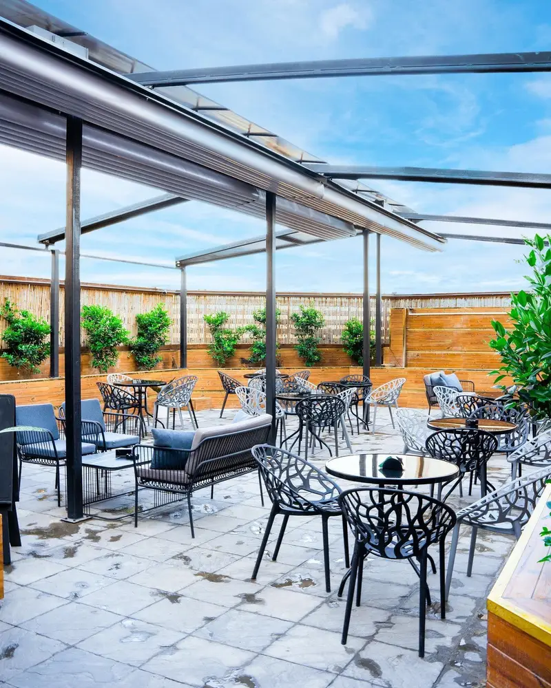 فضای باز دلپذیر کافه رستوران لاماسو با سقف متحرک، میز و صندلی های مدرن و چیدمان متنوع مناسب دورهمی ها.