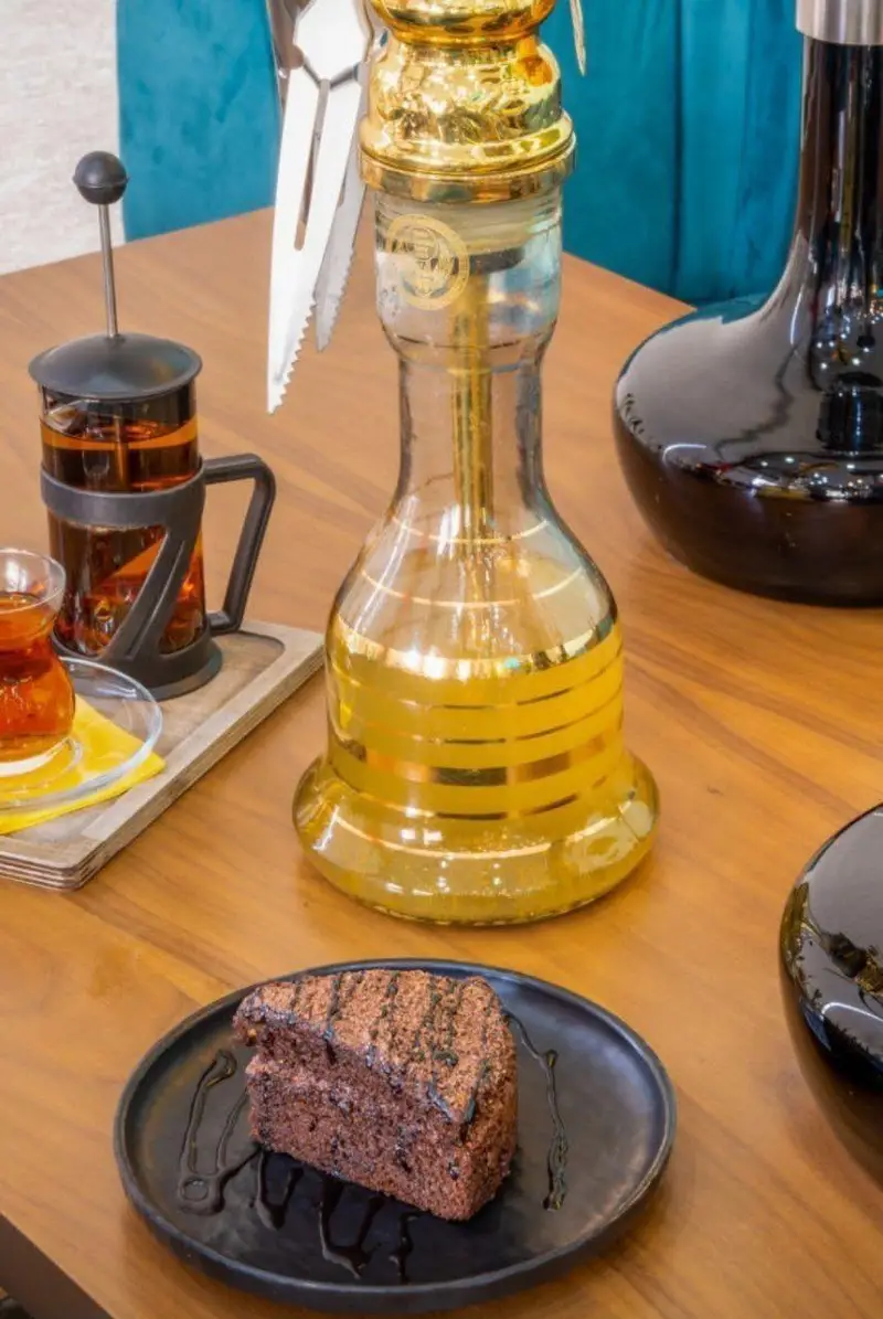 تصویری از میز کافه رستوران لاماسو با قلیان لوکس طلایی، چای تازه دم در فرنچ پرس و کیک شکلاتی خوشمزه. محیط آرام و دلپذیر کافه برای تجربه ای خاص.