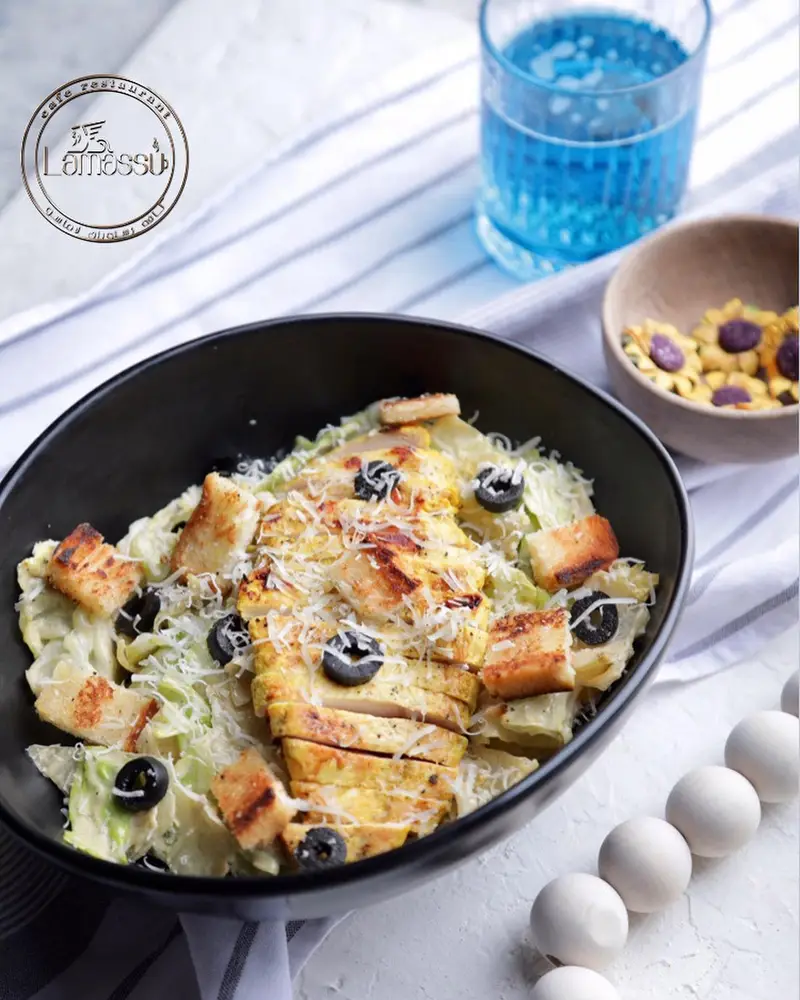 یک کاسه سالاد سزار با مرغ گریل، زیتون و نان سیر در کافه رستوران لاماسو، همراه نوشیدنی و شیرینی، انتخابی سالم.