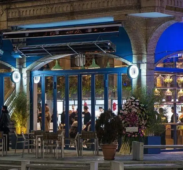 تصویری از نمای بیرونی فست فود و کافه تومو در شب با طراحی آبی، فضای نشستن در فضای باز و نورپردازی جذاب.