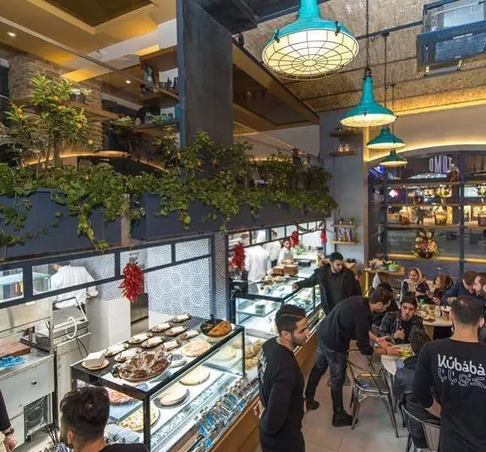 فضای داخلی وسیع و دلپذیر فست فود تومو، مملو از مشتریان، با دکوراسیون سبز، دسرهای متنوع و غذاهای تازه آماده.