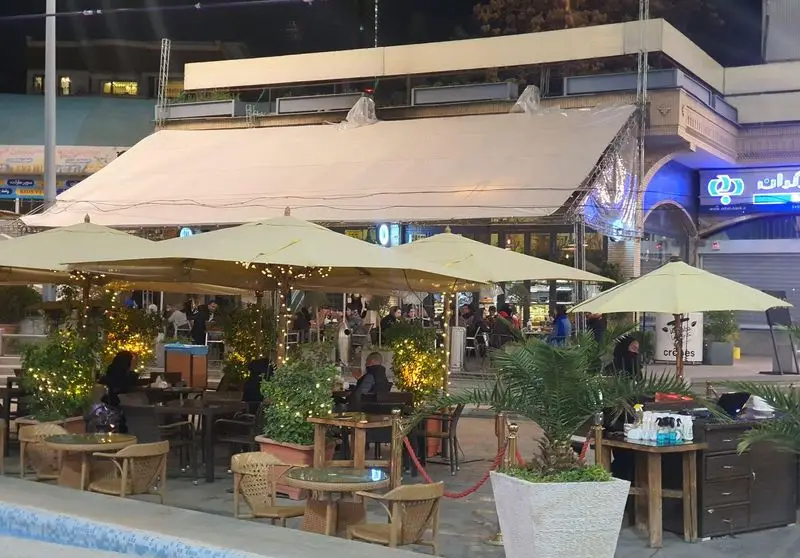 فضای باز دلنشین فست فود تومو در شب با میز و صندلی‌های راحت، چترهای بزرگ و نورپردازی زیبا برای مشتریان گرامی.