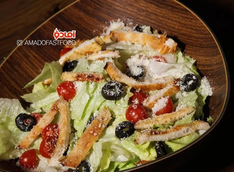 سالاد سزار مرغ تازه و خوشمزه فست فود پیلوت با کاهوی ترد، مرغ گریل شده، گوجه گیلاسی، زیتون سیاه و پنیر پارمزان.