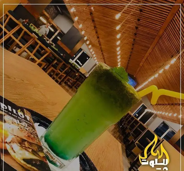 نوشیدنی گوارای سبز رنگ و خنک با نی زرد در فست فود پیلوت. فضای دلنشین رستوران با دکور چوبی، نورپردازی گرم و منوی وسوسه‌انگیز برگر پیلوت.