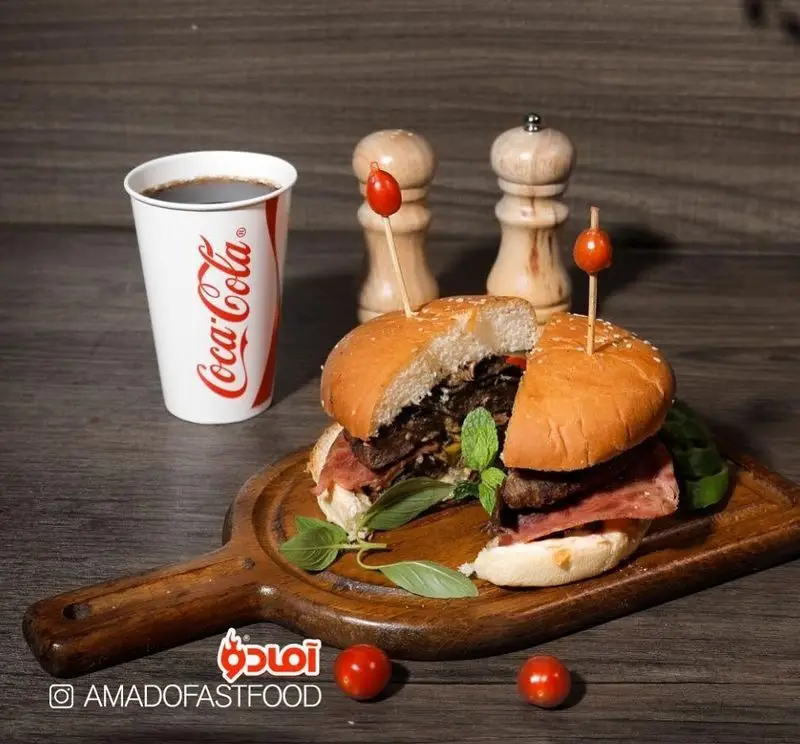 همبرگر ویژه فست فود پیلوت، برش خورده با مخلفات تازه و نوشیدنی کوکاکولا، روی تخته سرو چوبی. انتخابی عالی برای غذای شما.