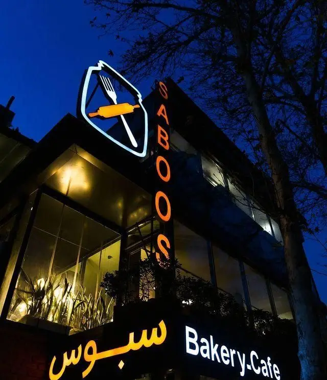 نمای بیرونی کافه نانوایی و رستوران سبوس در شب، با تابلوی نورانی Saboos و لوگوی چنگال و وردنه، فضایی مدرن و دلنشین.