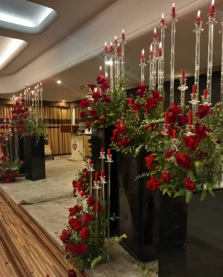 دکوراسیون مجلل و شیک مراسم با گل آرایی رز قرمز، شمعدان‌های بلند کریستالی و ظروف کرایه لوکس بلادی برای تشریفات عروسی.