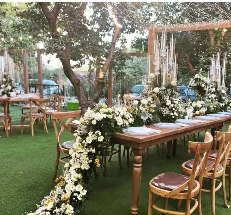 چیدمان شیک باغ با میز و صندلی چوبی کرایه ای بلادی، گل آرایی سفید و شمع، مناسب عروسی و مراسم در فضای باز. تجهیزات کامل مجالس.