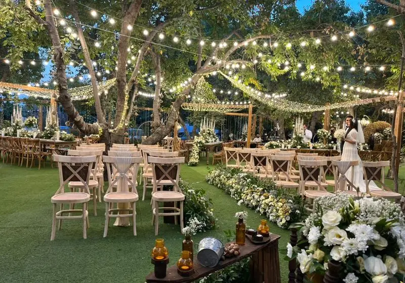 تصویر مراسم عروسی باشکوه در باغ با صندلی و میزهای اجاره ای، تزئینات گل آرایی و نورپردازی رمانتیک، ارائه شده توسط ظروف کرایه بلادی.
