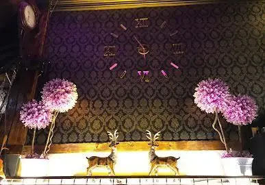 دکوراسیون داخلی شیک سفره خانه شهرزاد: ساعت دیواری رومی، گوزن‌های دکوری و گل‌های بنفش، فضایی سنتی و دلنشین.