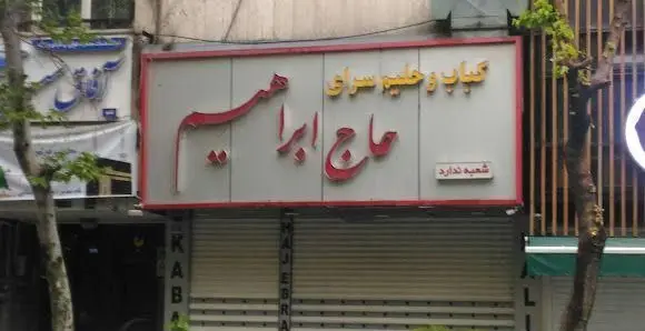 نمای بیرونی و تابلو سردر کبابی و حلیم سرای حاج ابراهیم با حروف برجسته قرمز و زرد رنگ، کسب و کار غذاخوری سنتی در تهران.