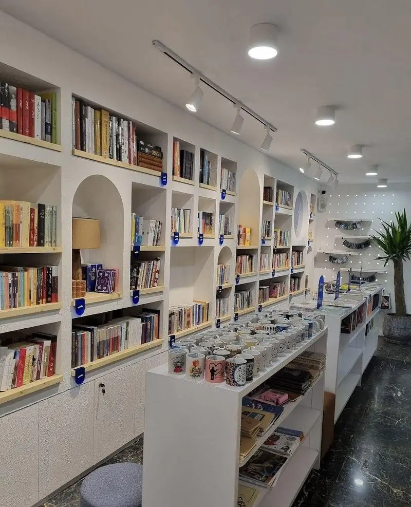 فضای داخلی دنج کافه کتاب ماه با قفسه‌های بلند کتاب، ماگ‌های زیبا و نورپردازی مدرن برای مطالعه و استراحت.