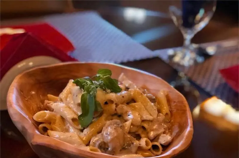 تصویری جذاب از پاستا پنه با سس آلفردو خامه ای، قارچ و تکه های مرغ، تزئین شده با ریحان تازه در کاسه چوبی. لذت غذا در کافی شاپ مازراتی.