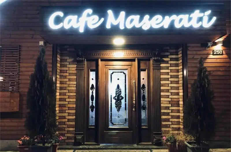 تصویری از نمای شب کافی شاپ مازراتی با تابلوی نئونی درخشان، ورودی مجلل چوبی و آجری، گلدان‌های درختی و شماره ۲۵۰