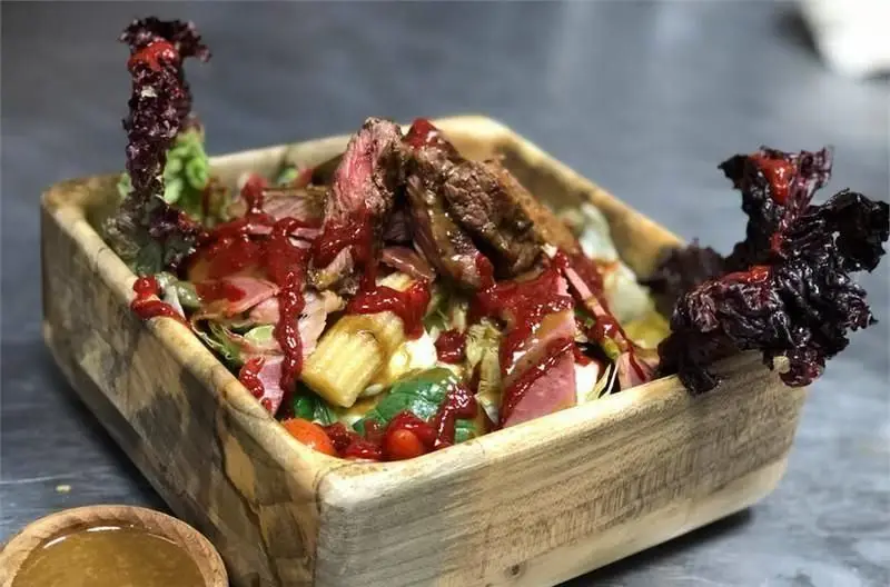 سالاد استیک مجلل و تازه با سس مخصوص، سبزیجات رنگارنگ و گوشت گریل در کاسه چوبی، تجربه‌ای بی‌نظیر در کافی شاپ مازراتی.