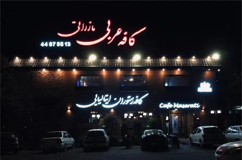 نمای شب از کافه مازراتی، یک کافی شاپ و رستوران عربی و ایتالیایی، با تابلوهای نئون و شماره تماس ۴۴۸۷۹۵۱۳.